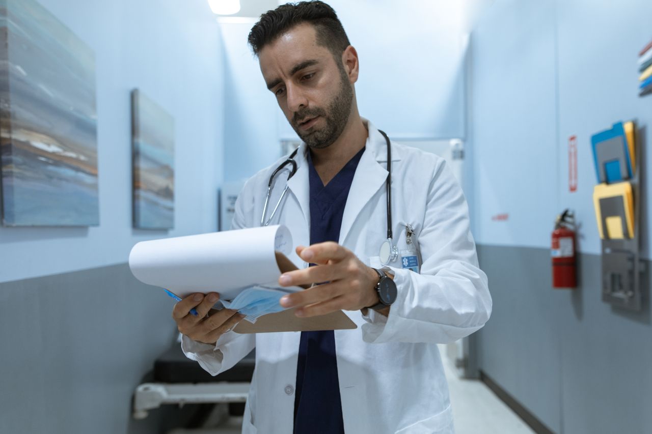 Portfolio Male doctor in hospital hallway reviewing medical charts, focused and dedicated.
